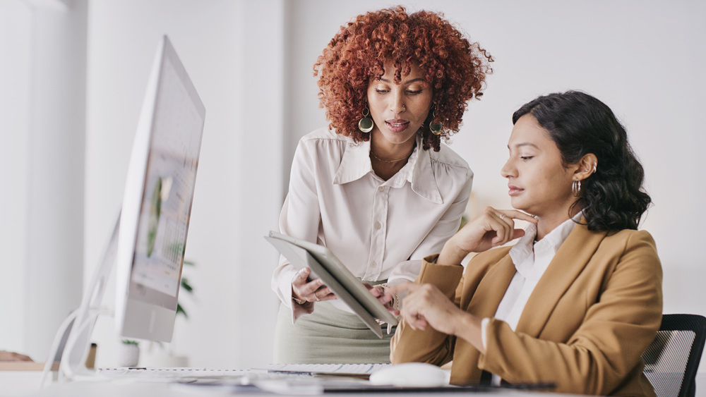 female secretary and leader talking while reviewing information on a tablet