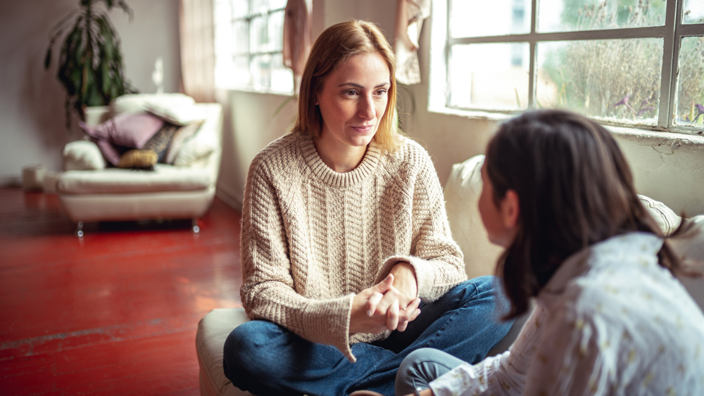 a mother and teenager daughter sitting on couch by window talking