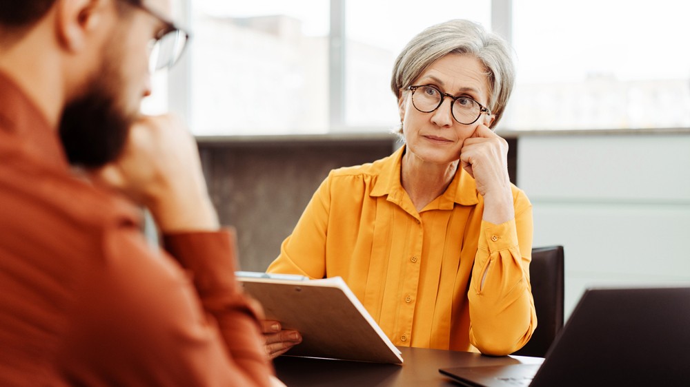 senior woman and younger man having serious talk in office