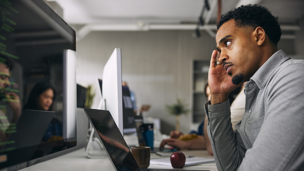 concerned male employee touching temple while sitting with laptop at office desk