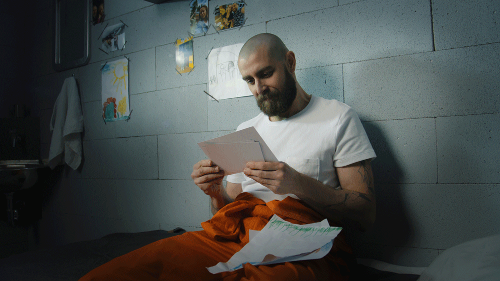 Inmate looks at family photos and kids drawings in prison cell