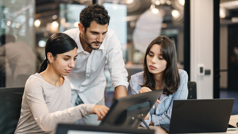 Group of business people working, the team are sitting at a board room table looking at a laptop computer.