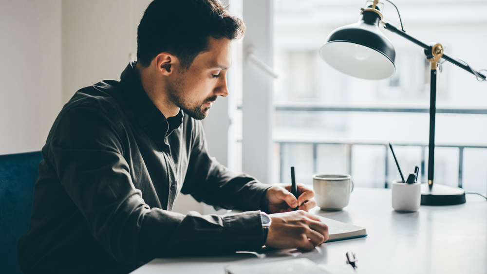 Businessman writing in notebook at home