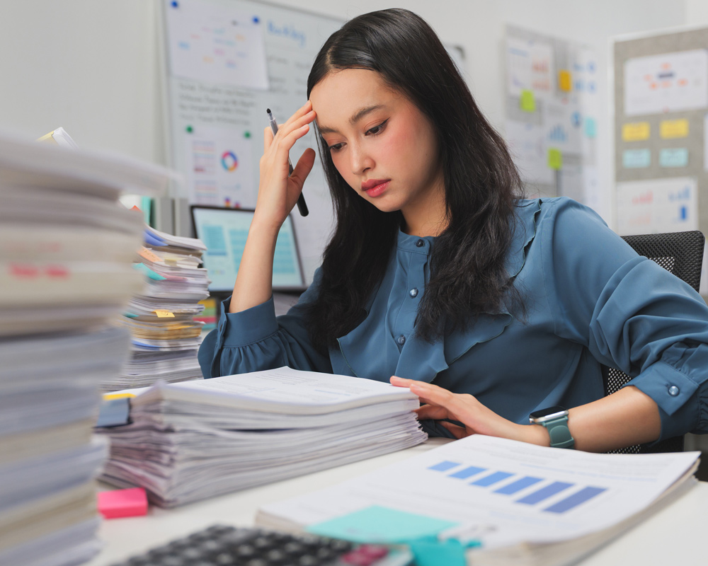 Overwhelmed woman reading a tall stack of paperwork