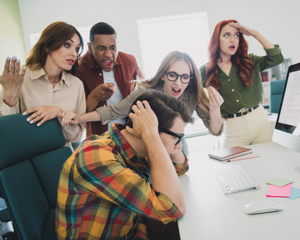 Stressed employee at a desk surrounded by arguing coworkers